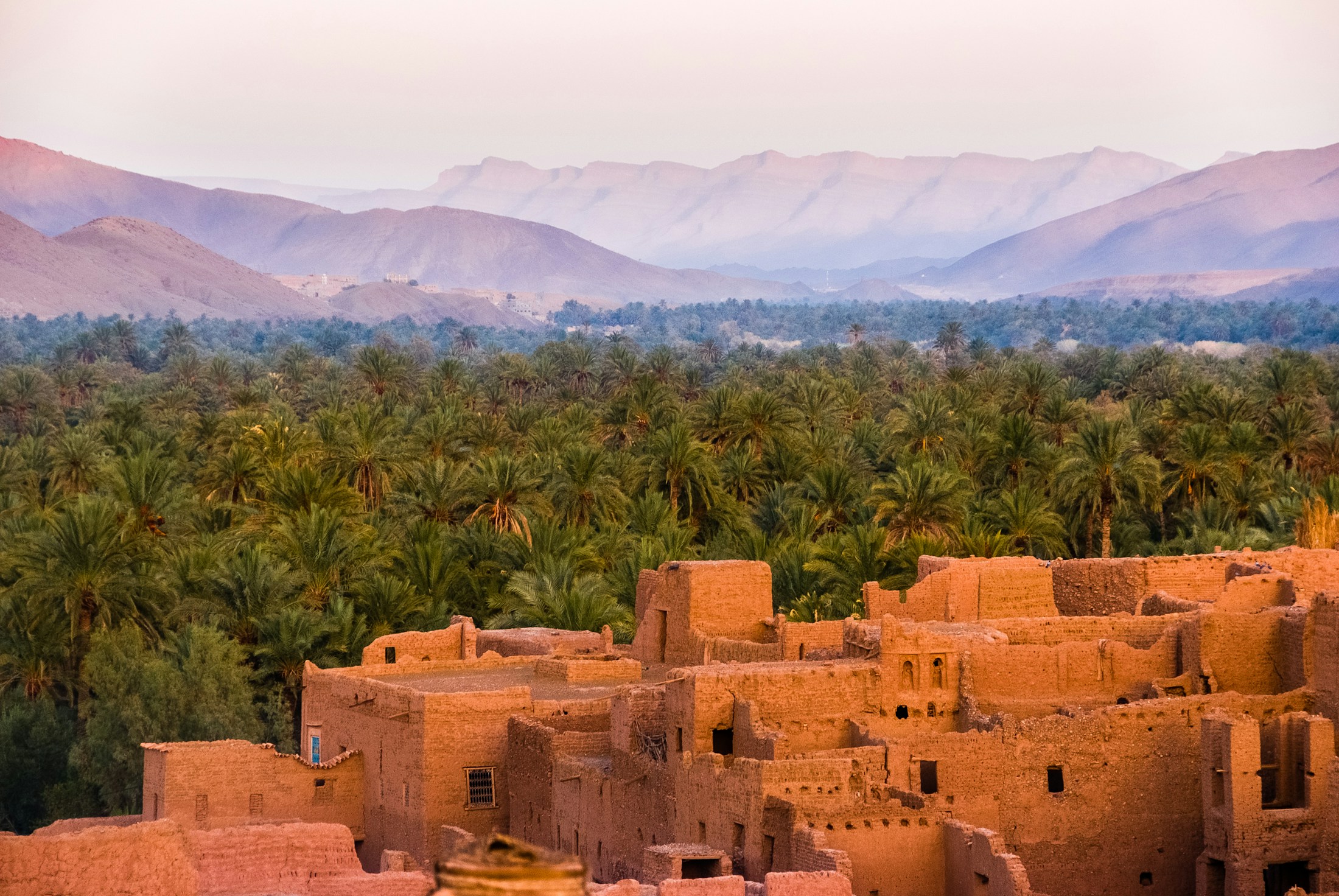 Sunlit Moroccan kasbah overlooking a lush palm oasis and distant mountains